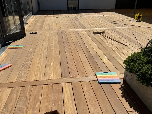 Terrasse af brede træplanker ved en glasdør, med værktøj og en plante i en stor krukke